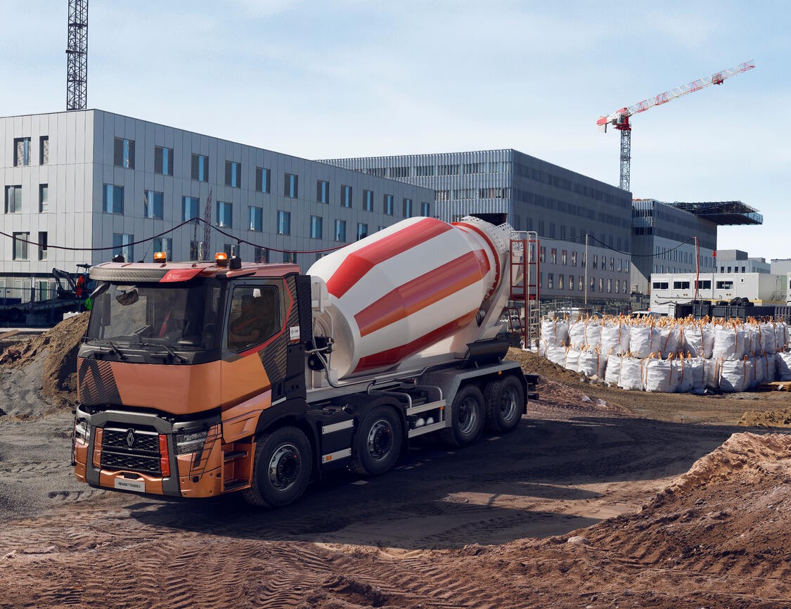A Renault Trucks C lorry fitted with a concrete mixer is operating on a large urban construction site surrounded by cranes and modern buildings.
